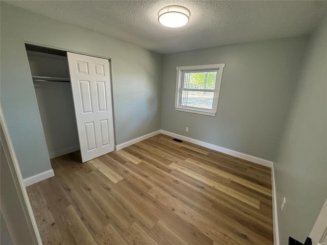 unfurnished bedroom featuring wood finished floors, a closet, a textured ceiling, and visible vents