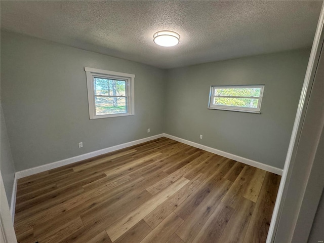 empty room featuring baseboards, a textured ceiling, plenty of natural light, and wood finished floors