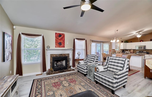 living room with a wealth of natural light, ceiling fan with notable chandelier, a fireplace, and light wood-type flooring