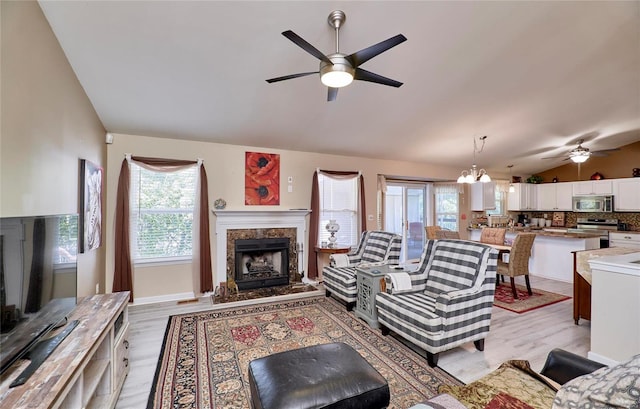 living room featuring light hardwood / wood-style floors, a premium fireplace, lofted ceiling, and ceiling fan with notable chandelier