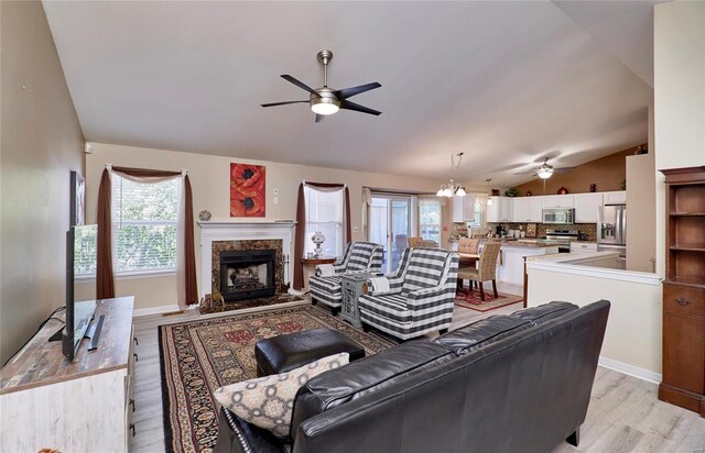 living room featuring ceiling fan with notable chandelier, light hardwood / wood-style floors, vaulted ceiling, and a fireplace