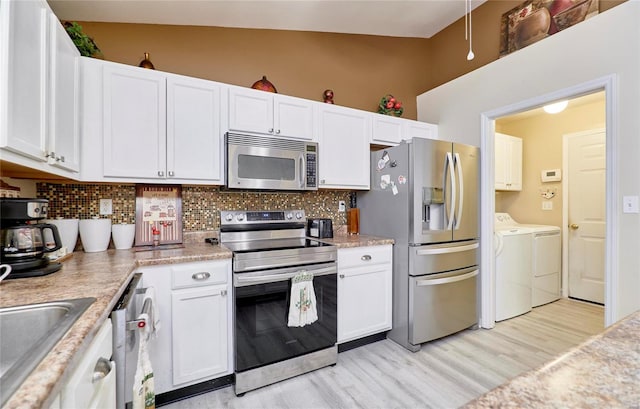 kitchen with lofted ceiling, independent washer and dryer, stainless steel appliances, light wood-type flooring, and white cabinetry