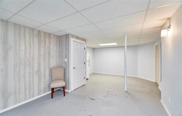 basement with a paneled ceiling, wood walls, and white refrigerator