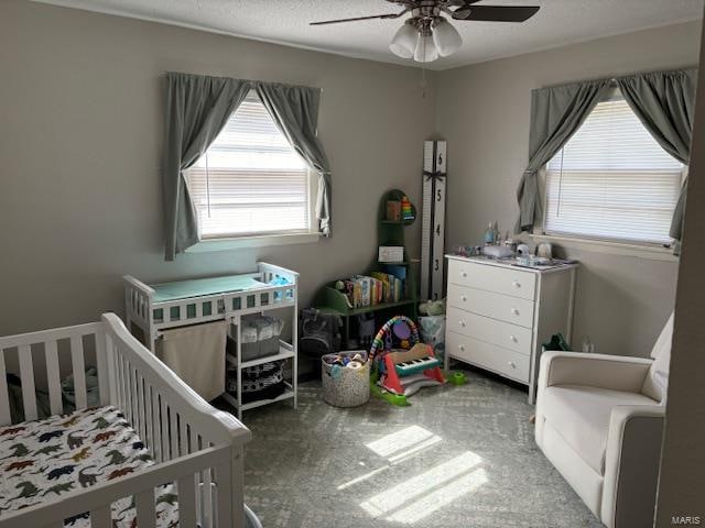 carpeted bedroom featuring ceiling fan, a nursery area, and a textured ceiling