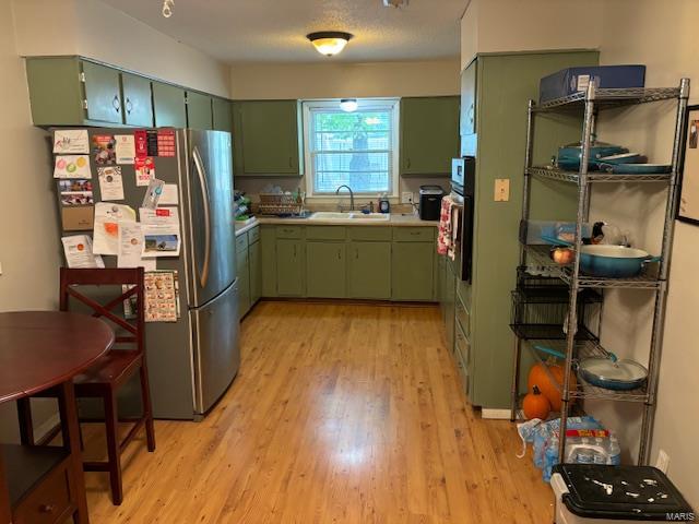 kitchen with light hardwood / wood-style floors, stainless steel refrigerator, green cabinetry, and sink