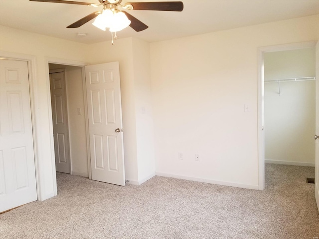 unfurnished bedroom featuring ceiling fan, a closet, a spacious closet, and light colored carpet