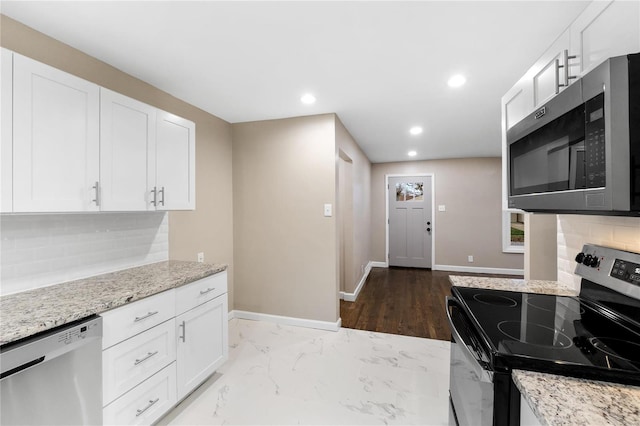 kitchen with white cabinets, backsplash, light stone counters, and stainless steel appliances