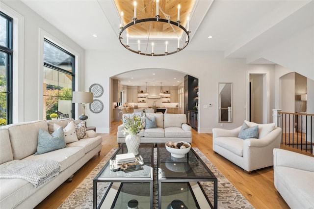 living room with an inviting chandelier, a high ceiling, light wood-type flooring, and wooden ceiling