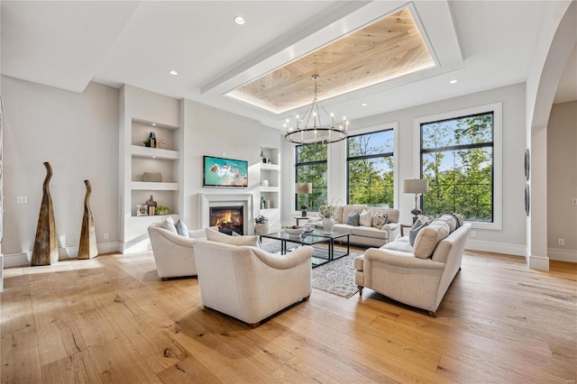 living room featuring light hardwood / wood-style floors, a notable chandelier, a tray ceiling, and built in shelves