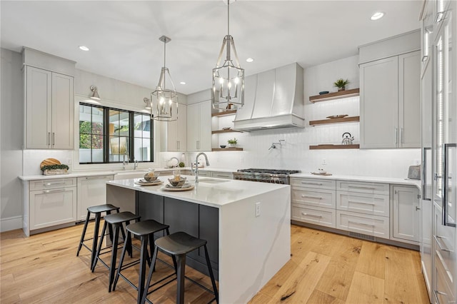 kitchen featuring light hardwood / wood-style flooring, sink, an island with sink, custom exhaust hood, and a breakfast bar