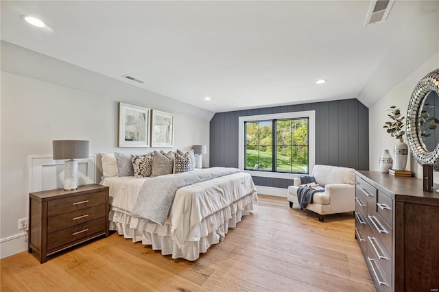 bedroom featuring lofted ceiling, wood walls, and light wood-type flooring