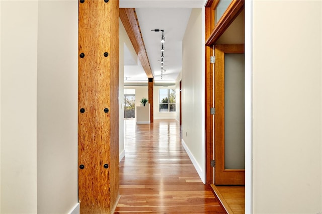 corridor with beamed ceiling, light wood-type flooring, and rail lighting