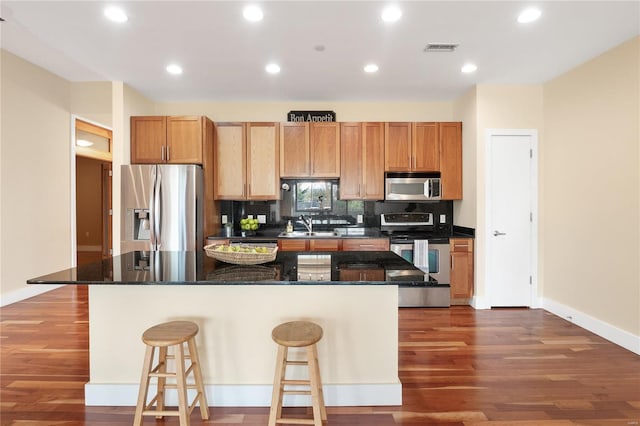 kitchen featuring dark stone counters, dark hardwood / wood-style flooring, a kitchen breakfast bar, appliances with stainless steel finishes, and a center island