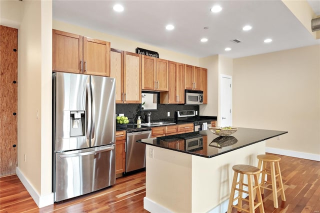 kitchen featuring sink, a kitchen island, stainless steel appliances, a breakfast bar area, and light wood-type flooring