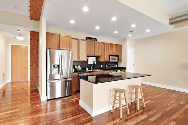 kitchen with appliances with stainless steel finishes, a kitchen island, light hardwood / wood-style floors, and a kitchen breakfast bar