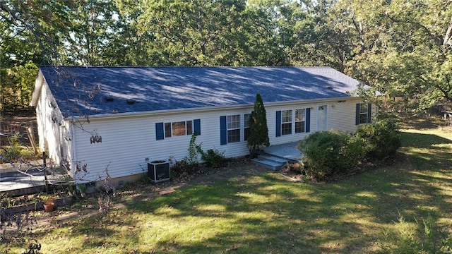 rear view of house with central AC unit and a yard