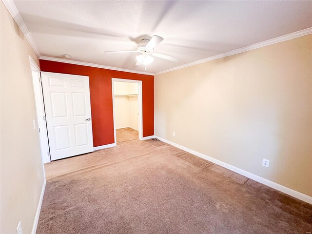 unfurnished bedroom featuring a spacious closet, ceiling fan, a closet, crown molding, and carpet floors