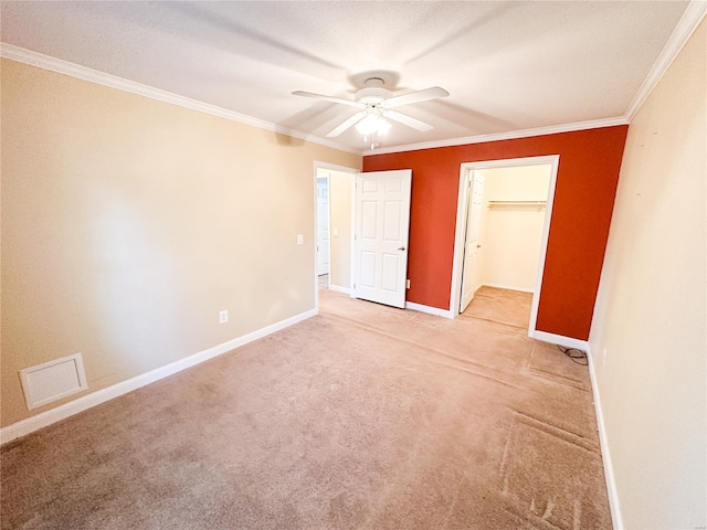 unfurnished bedroom featuring ceiling fan, ornamental molding, a closet, a spacious closet, and light carpet