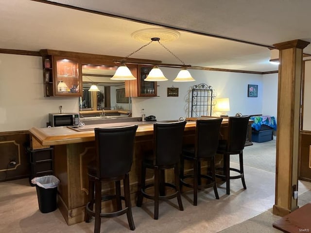 bar featuring crown molding, decorative light fixtures, and decorative columns