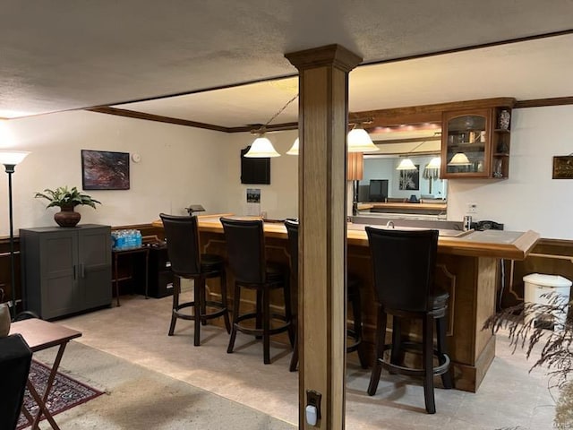 bar with ornate columns, light carpet, ornamental molding, decorative light fixtures, and a textured ceiling