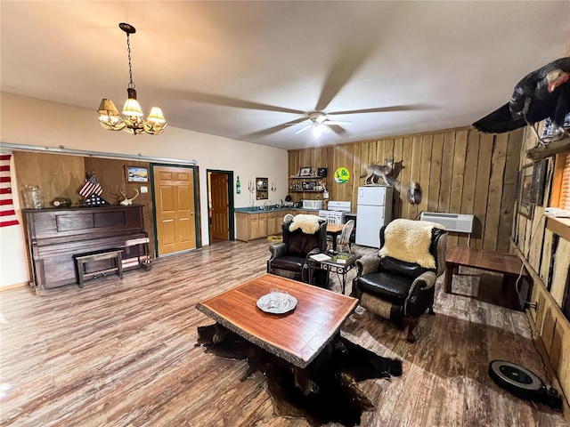 living room with wood walls, ceiling fan with notable chandelier, and light hardwood / wood-style floors