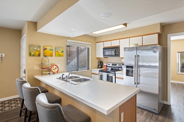 kitchen featuring stainless steel appliances, sink, a kitchen breakfast bar, white cabinets, and dark hardwood / wood-style flooring