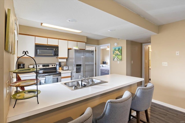 kitchen with sink, kitchen peninsula, appliances with stainless steel finishes, white cabinets, and dark hardwood / wood-style flooring