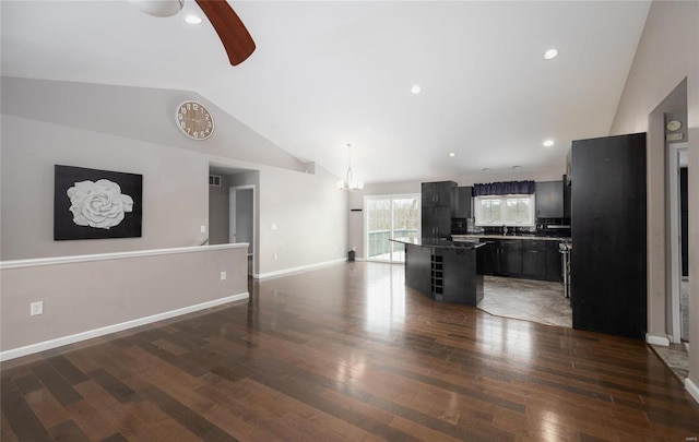 kitchen featuring a center island, vaulted ceiling, a kitchen bar, dark hardwood / wood-style floors, and ceiling fan with notable chandelier