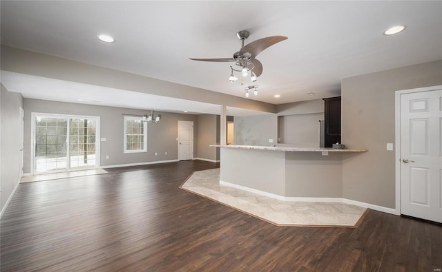 kitchen featuring kitchen peninsula, dark wood-type flooring, light stone countertops, and ceiling fan with notable chandelier