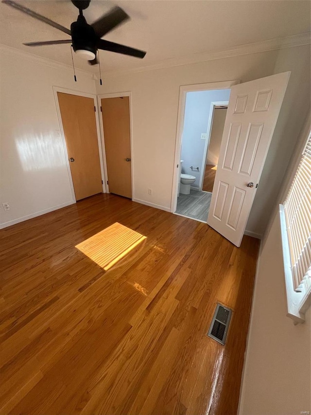 unfurnished bedroom featuring ceiling fan, hardwood / wood-style flooring, crown molding, ensuite bathroom, and a closet