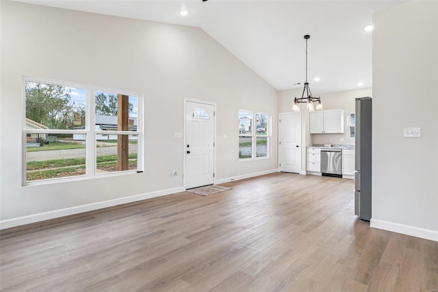 unfurnished living room featuring high vaulted ceiling, light wood-type flooring, and an inviting chandelier