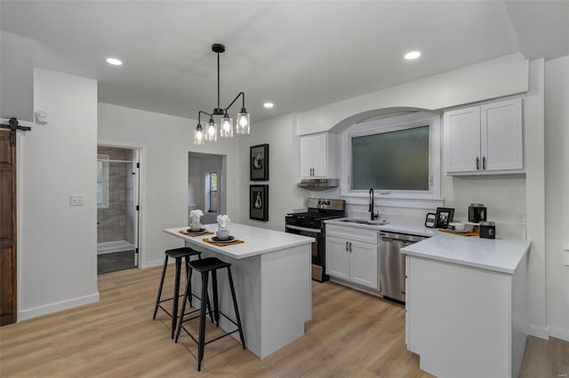 kitchen featuring stainless steel appliances, sink, a barn door, decorative light fixtures, and white cabinets