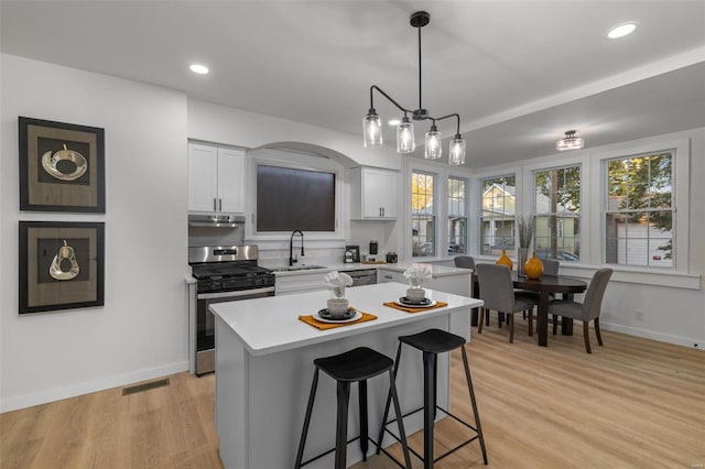 kitchen featuring white cabinets, light wood-type flooring, stainless steel appliances, decorative light fixtures, and a center island