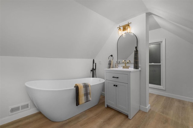 bathroom with vanity, a tub, wood-type flooring, and vaulted ceiling