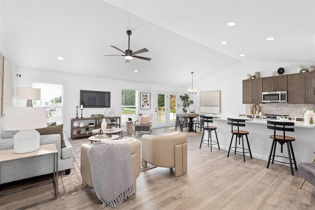 living room with ceiling fan with notable chandelier, a healthy amount of sunlight, vaulted ceiling, and light hardwood / wood-style floors