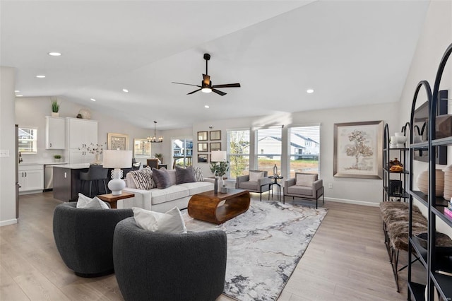 living room with ceiling fan with notable chandelier, lofted ceiling, and light hardwood / wood-style floors