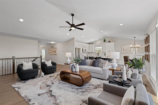 living room featuring lofted ceiling, wood-type flooring, and ceiling fan with notable chandelier