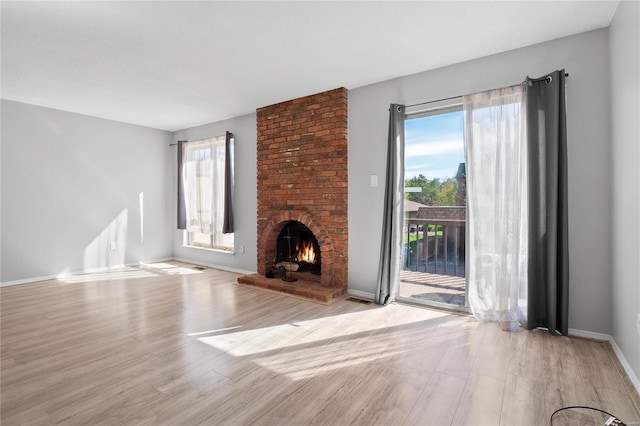 unfurnished living room featuring a brick fireplace, light hardwood / wood-style floors, and plenty of natural light