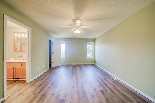 unfurnished bedroom featuring a textured ceiling, ensuite bathroom, light hardwood / wood-style floors, and ceiling fan