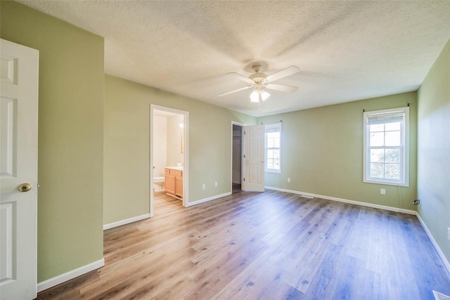 unfurnished bedroom with light hardwood / wood-style flooring, multiple windows, connected bathroom, and ceiling fan