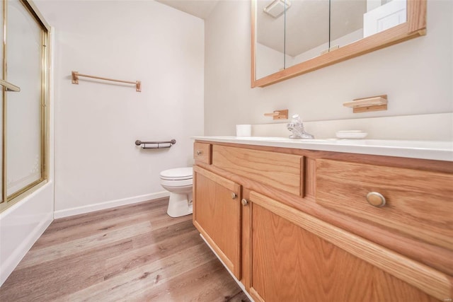 full bathroom with vanity, bath / shower combo with glass door, hardwood / wood-style flooring, and toilet