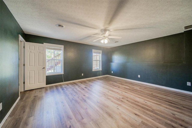 empty room with ceiling fan, a textured ceiling, light wood-type flooring, and plenty of natural light