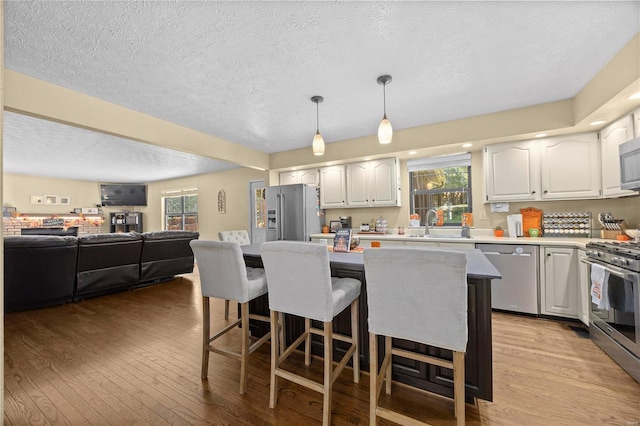 kitchen with light wood-type flooring, hanging light fixtures, white cabinetry, a breakfast bar area, and appliances with stainless steel finishes