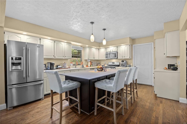 kitchen with appliances with stainless steel finishes, white cabinetry, a center island, and dark hardwood / wood-style floors