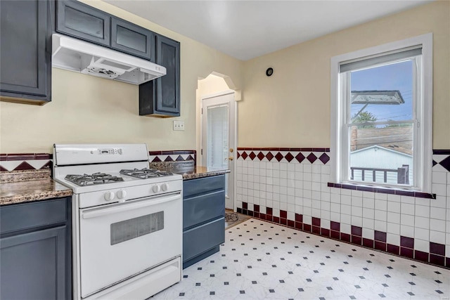 kitchen featuring tile walls, white range with gas cooktop, and gray cabinets