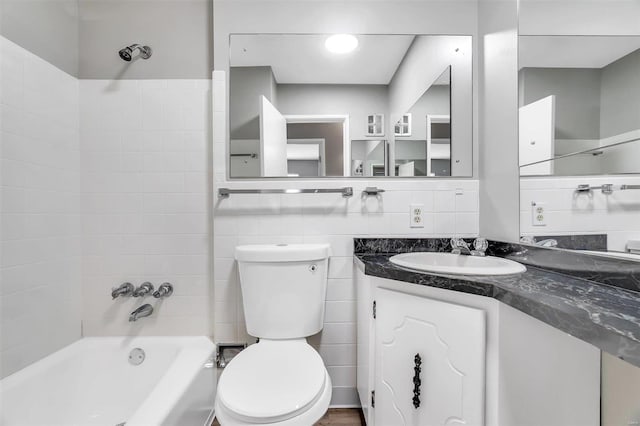 full bathroom featuring tiled shower / bath, vanity, toilet, and tile walls