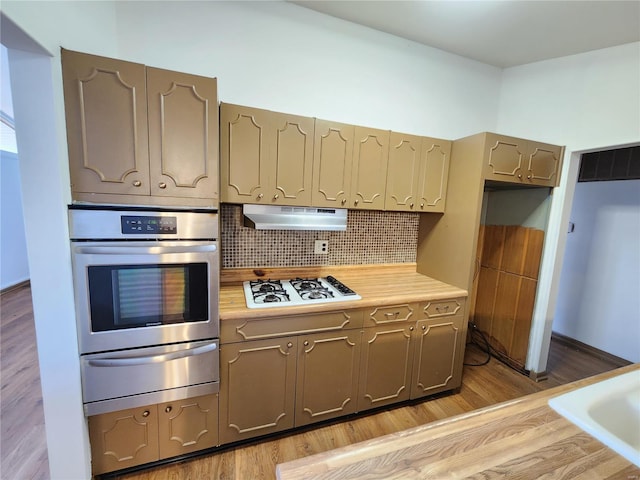 kitchen featuring stainless steel oven, light wood-type flooring, white gas stovetop, and tasteful backsplash