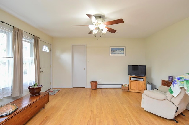 living area featuring ceiling fan, light wood-type flooring, and a baseboard heating unit