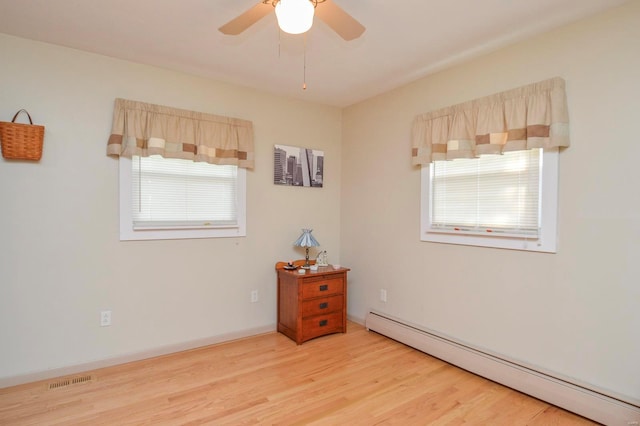 spare room featuring ceiling fan, light wood-type flooring, plenty of natural light, and a baseboard heating unit