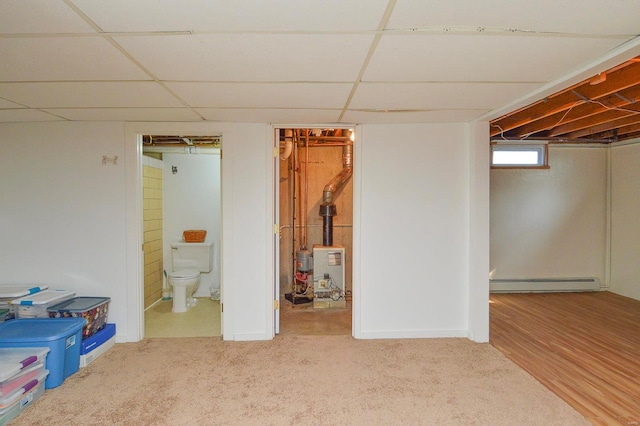 basement featuring a drop ceiling, a baseboard heating unit, and carpet